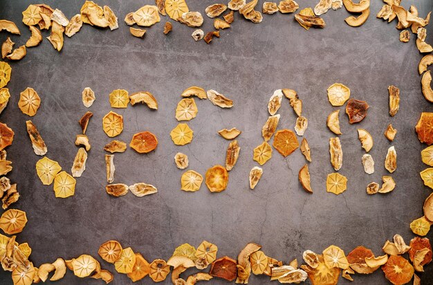 Inscription vegan from pieces of dried fruits in a fruit frame on a dark background