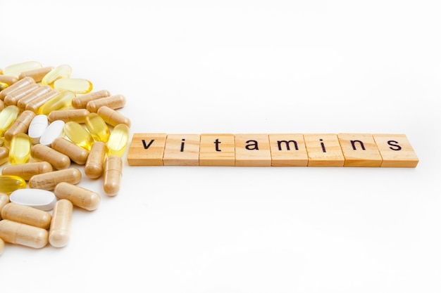 Photo inscription vitamins in wooden cubes on a white background of different pills