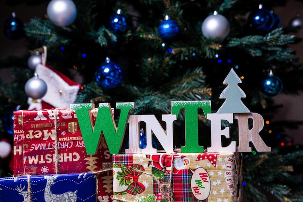 Надпись зима с елки на Новый год На еловых ветках на фоне снежного покрова новогодние бело-голубые шары с еловыми шишками и коробка с подарком рождеством