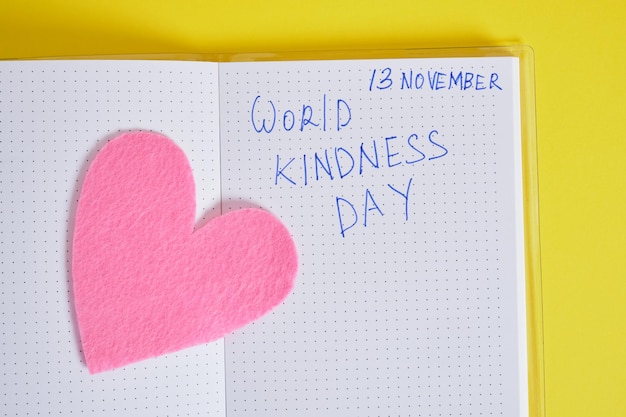 Надпись всемирный день доброты в блокноте и войлочное сердце на желтом фоне