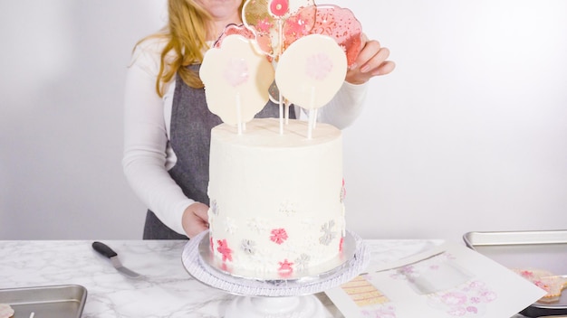 Inserting large lollipops with snowflakes into the tall white round cake as a final decoration.