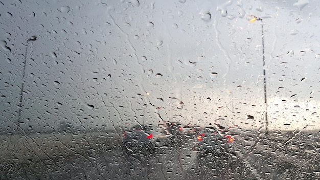 車内。クローズアップ雨水滴。夕方の高速道路で雨の日の車のフロントガラスのビュー