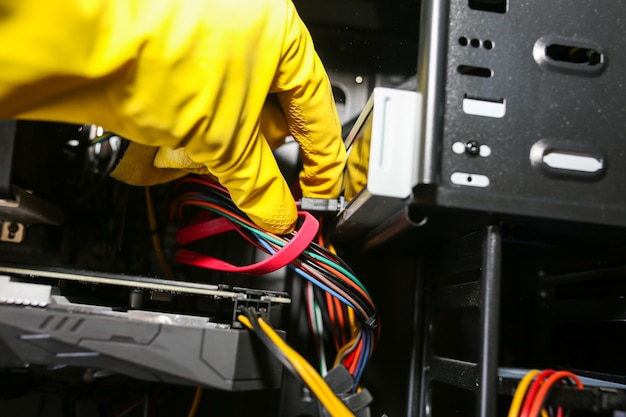 Dettagli interni del personal computer. l'uomo sta pulendo i fili in guanti gialli. scheda madre e scheda video nella polvere. pc rotto.