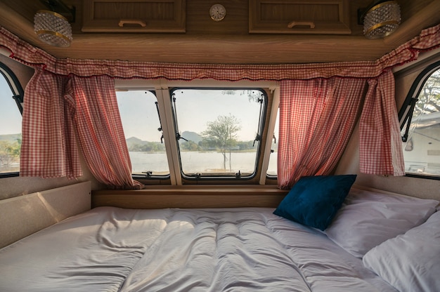 Foto all'interno del letto vuoto in camper e la vista attraverso la finestra con tenda sul lago