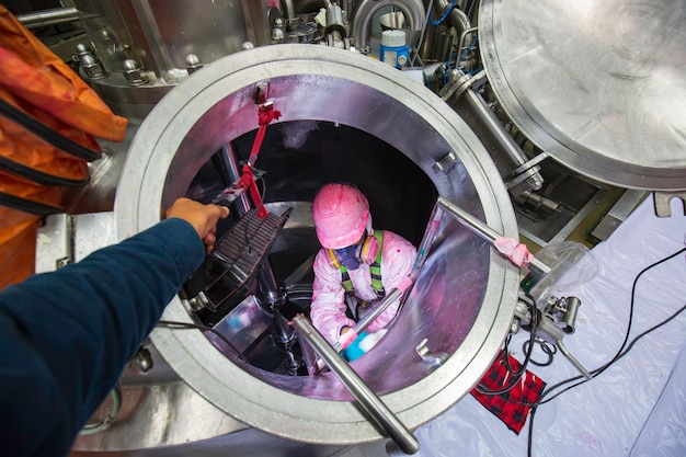 Inside male two worker into the inspection shiny tank stainless chemical  blower fresh air into area confined space.