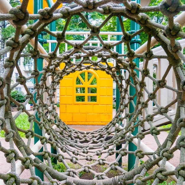 Inside view of a long rope mesh pipe at the end of the tunnel yellow playground blurred background