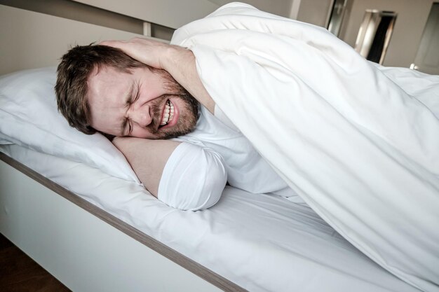 Foto l'uomo insonnia non riesce ad addormentarsi a causa dello stress da rumore e dell'ansia, si copre le orecchie con le mani