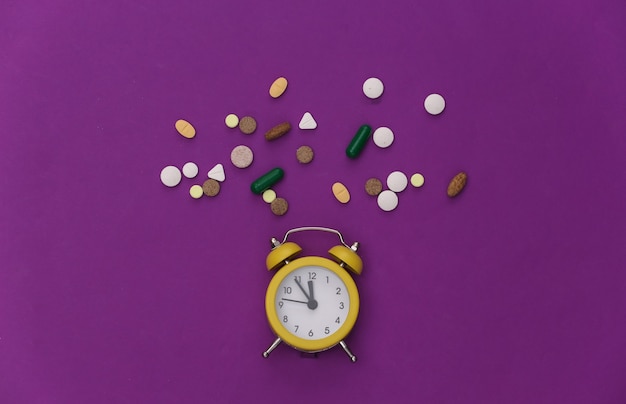 Insomnia. Mini alarm clock and pills on a purple background..