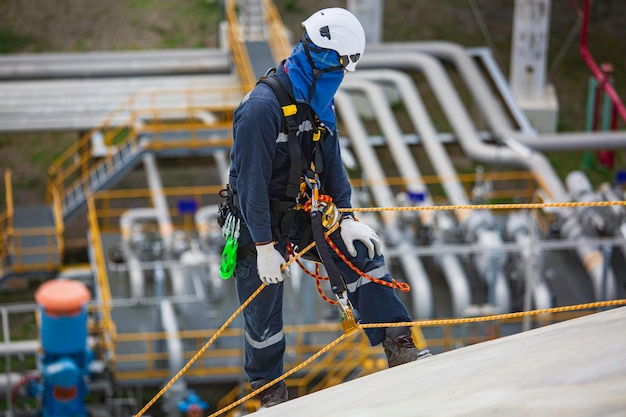 Inspectie van mannelijke werknemers met een veiligheidslijn met veiligheidsharnas die op een hoge plaats op een bolvormig gas op het tankdak werkt