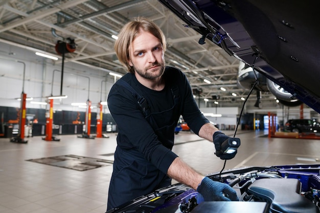 Ispezione dell'auto presso la stazione di servizio meccanico di auto maschio barbuto durante la risoluzione dei problemi sotto il cofano