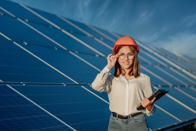 Ispettore ingegnere donna che tiene la tavoletta digitale lavorando in pannelli solari power farm, parco di celle fotovoltaiche, concetto di energia verde.