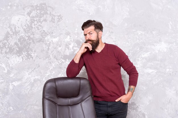 Inspiratie nodig voor kantoorgarderobe Serieuze hipster staat op stoel Bebaarde man draagt casual stijl Casual herenoutfit Casual herenkleding Casual en comfortabel