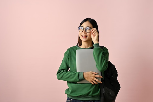 Inspired Asian female college student touching her glasses holding her laptop