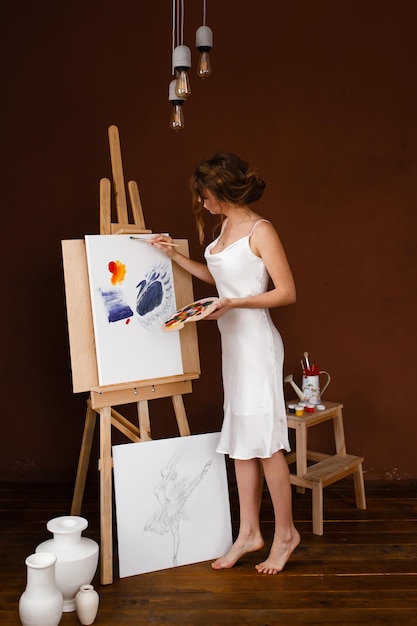 Inspired by the beautiful sensual girl artist draws a picture in the white dress stained with paint