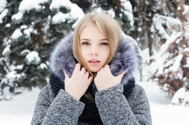 Inspired caucasian woman in woolen scarf looking away with smile while posing in winter morning. Close-up portrait fascinating female standing in snowy yard. Cold sunny weather. Woman winter concept.