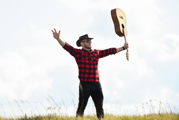 Musicista country ispirato stile country vacanze estive canzone escursionistica uniti con la natura bell'uomo con chitarra concetto di musica country il cantante country del chitarrista stand sullo sfondo del cielo di campo