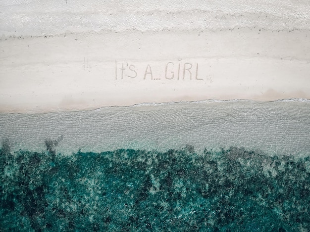 Inspired future father wrote a phrase "It's a girl" on the sand by turquoise waters, aerial view.