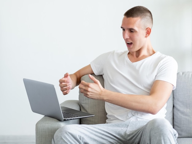 Inspired information Emotional man Online meeting Surprised excited casual guy sitting sofa talking on laptop gesturing hands in light room interior