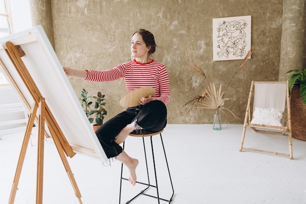 Inspired woman painting on easel with brush