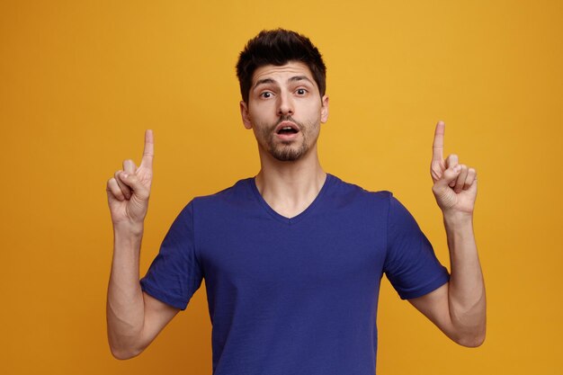 Inspired young handsome man looking at camera pointing fingers up on yellow background