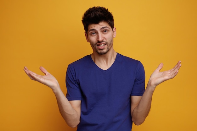 Inspired young handsome man looking at camera showing empty hands on yellow background