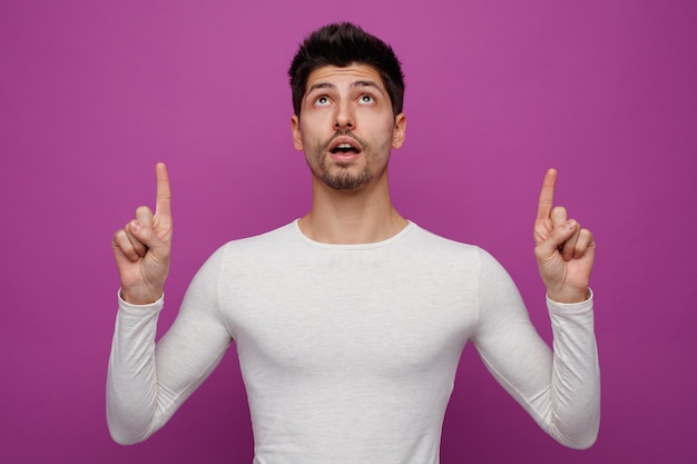 Inspired young handsome man pointing and looking up on purple background