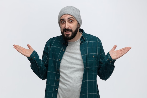 Inspired young man wearing winter hat looking at camera showing empty hands isolated on white background