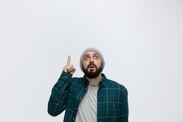 Inspired young man wearing winter hat looking and pointing up isolated on white background with copy space