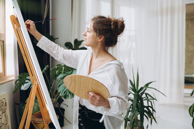 Inspired young woman in white shirt and black pants using brush and color palette