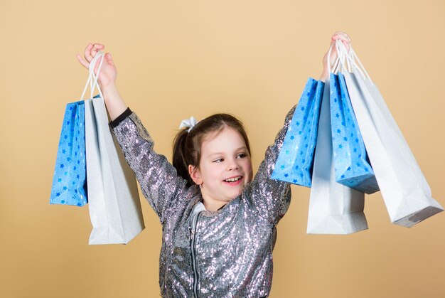 ショッピングバッグベージュの背景を持つ女の子をもっと購入するための刺激的な店ショッピングとブラックフライデーの購入セール割引ショッピングの日子供は束のパッケージを保持しますキッズファッションサプライズギフト