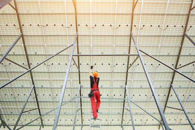 Installatie en bedrading van fotovoltaïsch zonnepaneel werknemer in oranje uniform verbindt zonnepanelen op het station