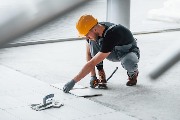 Installatie van platen Man in grijs uniform en oranje helm werkt overdag binnenshuis in een modern groot kantoor