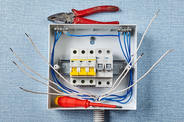 Installation of a household electrical panel or fusebox with automatic fuses. A repairman left a working tool on a switchboard or distribution board. Installing of circuit breakers in home wiring.