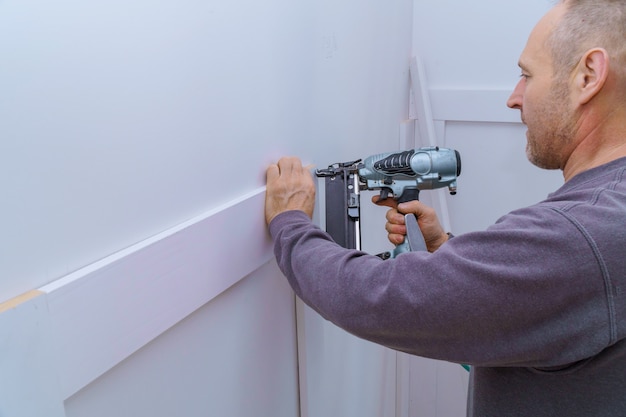 Photo installation mouldings on the wall of fragment of molding, top view of carpenter using nail gun