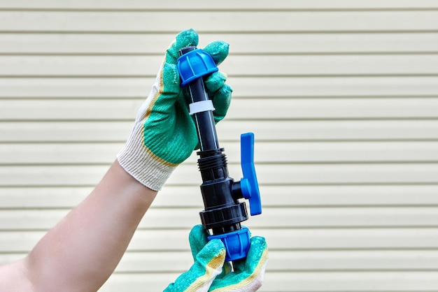 Photo installation of pipeline joint with ball valve using compression clamps gloved hands on striped background of house wall