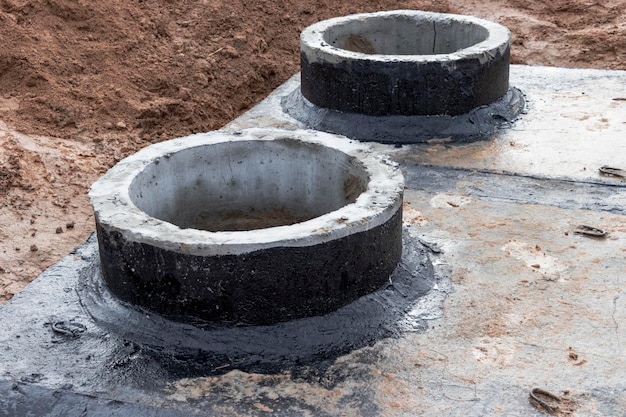 Монтаж железобетонного колодца для водоснабжения и канализации на стройплощадке Колодезные кольца с чугунным люком и строительным инструментом