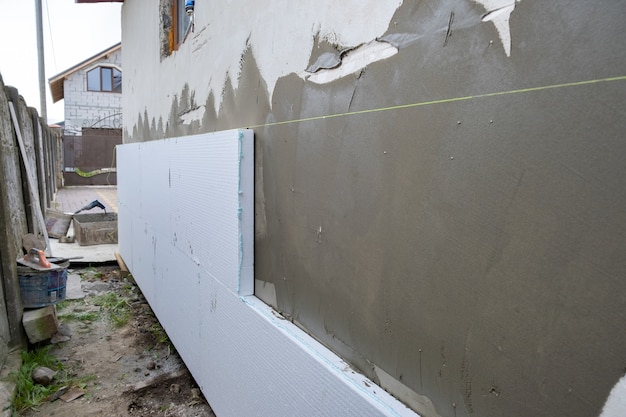 Installation of styrofoam insulation sheets on house facade wall for thermal protection.