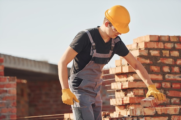 写真 レンガの壁を設置する建設作業員を制服と安全装置に設置するのは建物の仕事です