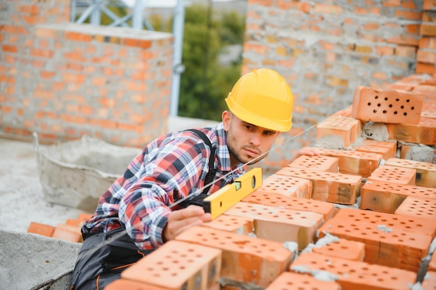 写真 レンガの壁を設置する建設作業員を制服と安全装置に設置するのは建物の仕事です