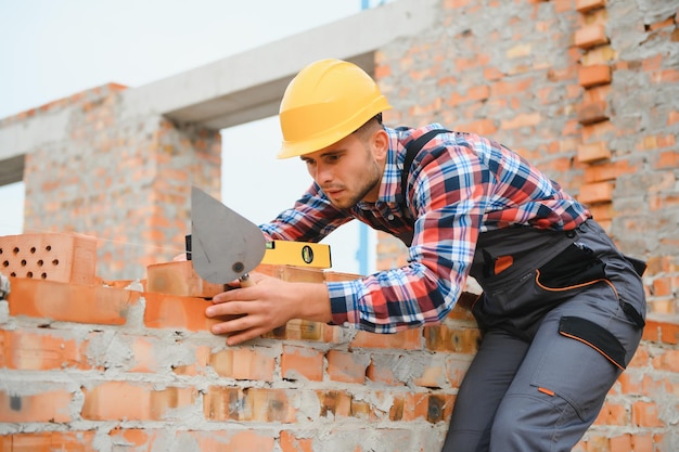 レンガの壁を設置する建設作業員を制服と安全装置に設置するのは建物の仕事です