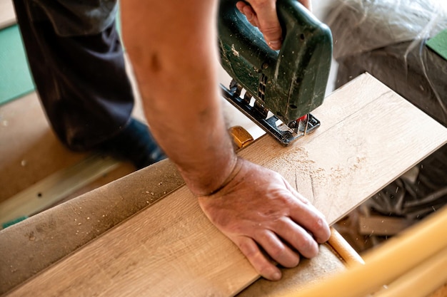 Foto installando il pavimento laminato, il lavoratore taglia una parte del pannello con un puzzle elettrico