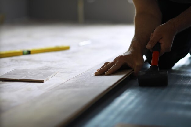 Installing laminated floor detail on man hands blue wooden tile over white foam base layer small pile with more tiles background