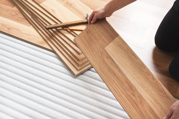 installing laminated floor, detail on man hands holding wooden tile, over white foam base layer