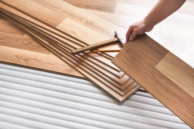 Installing laminated floor, detail on man hands holding wooden tile, over white foam base layer.