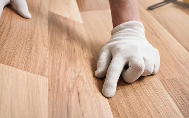 Installing laminated floor, detail on man hands in white gloves fitting wooden tile