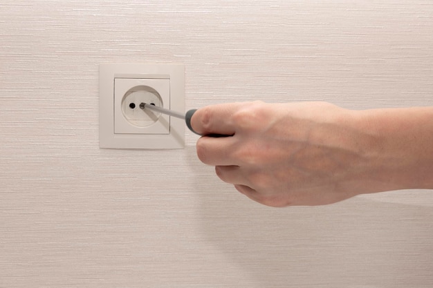 Installing an outlet with a screwdriver at home. A hand holds a screwdriver and screws a beige electrical outlet to the wall. High quality photo