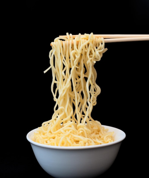 Instant Chinese curly noodles in white bowl with wood sticks on black background Selective focus Asian food concept Unhealthy eating