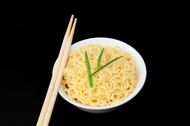 Instant Chinese curly noodles in white bowl with wood sticks on black background Selective focus Asian food concept Unhealthy eating