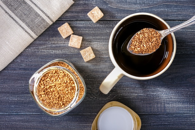 Instant coffee. Cup with hot water and instant coffee spoon, brown sugar on wooden table.