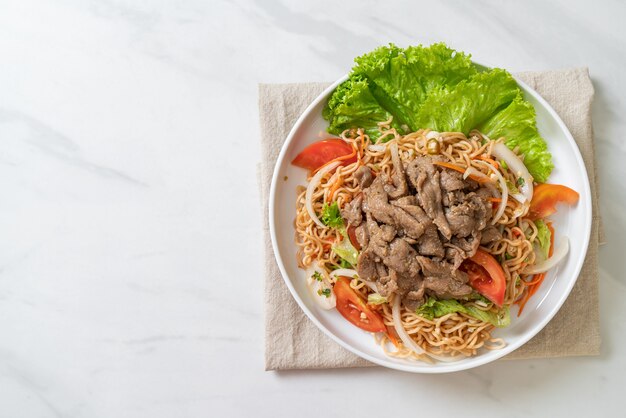 Insalata piccante di spaghetti istantanei con carne di maiale su piatto bianco. stile di cibo asiatico